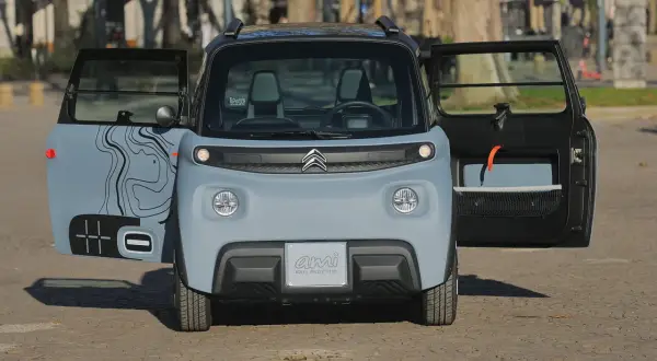 Citroën Ami 100% Electric, in prova, con portiere aperte e grafica stilizzata.