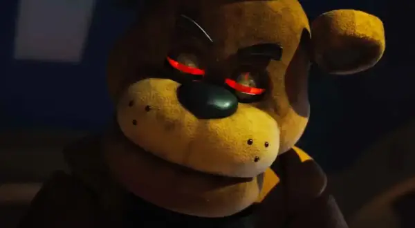 Freddy Fazbear z czerwonymi, świecącymi oczami, wygląda złowrogo w ciemności.