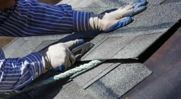 A roofer uses a utility knife to cut shingles, a step in how to dispose of shingles properly after removal.