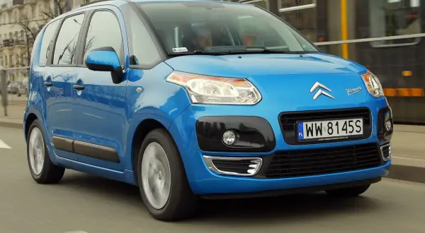Niebieski Citroen C3 Picasso 2009 jedzie ulicą, mijając tramwaj.