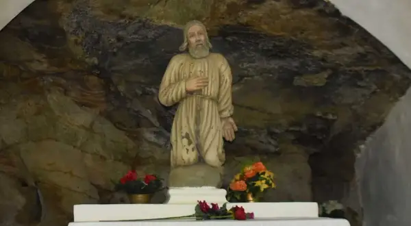 Kamienna grota, w której 13 lipca stoi figura świętego w zniszczonym habicie. Obok kwiaty.