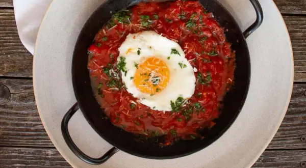 Ein Spiegelei ruht auf einer herzhaften, italienischen Tomatensauce, garniert mit Petersilie und Parmesan.
