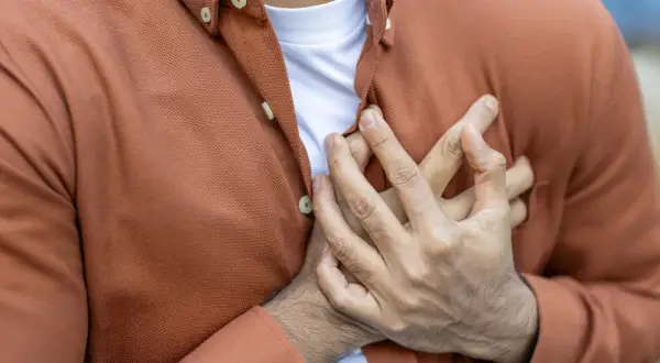 Mężczyzna trzyma się za serce, co może sugerować problemy związane z cholesterolem, np. wysoki poziom apolipoproteiny B.