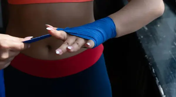 Une femme en tenue de sport prépare ses mains pour l'entraînement, montrant comment mettre des bandes de boxe bleues.