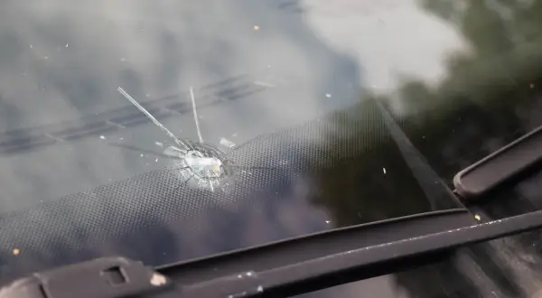 Gwiazdkowaty odprysk na przedniej szybie samochodu, z widocznymi pęknięciami i drobnymi odłamkami szkła.