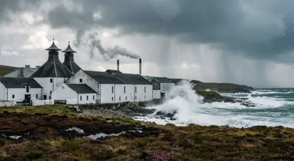 Distillerie sur l'île d'Islay, battue par les vagues et la pluie sous un ciel orageux. La fumée s'échappe d'une cheminée.