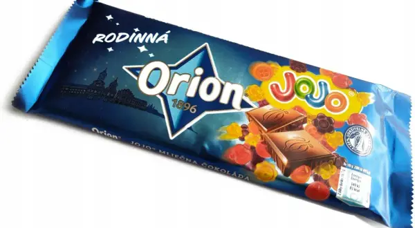 Orion Mléčná čokoláda z želkami. Kolorowe żelki w kształcie kwiatków i guzików otaczają kostki czekolady na opakowaniu.