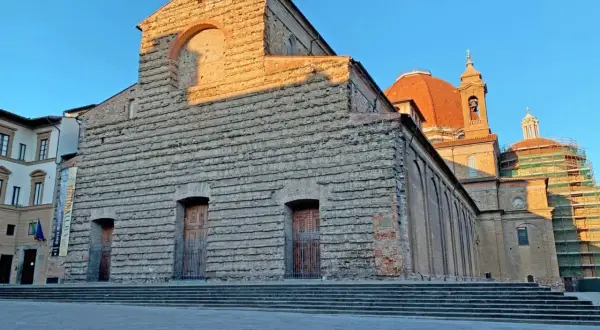 La Basilica di San Lorenzo a Firenze, con la sua facciata in pietra grezza e la cupola arancione, illuminata dal sole del tramonto.