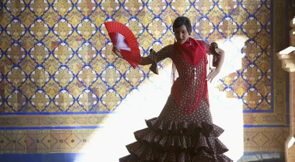 Tancerka w hiszpańskim stroju flamenco, z wachlarzem w dłoni, na tle zdobionej kafelkami ściany.