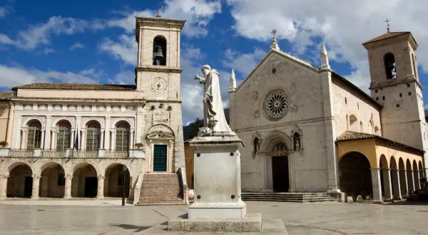 La piazza di Norcia con la basilica e il palazzo comunale, dominata dalla statua di San Benedetto. La basilica di Norcia oggi si presenta maestosa.