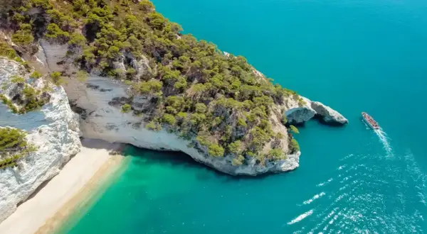 Piękna plaża i turkusowe morze, idealne miejsce, by zastanowić się, gdzie do Włoch na wakacje. Statek wycieczkowy zbliża się do skalistego wybrzeża.