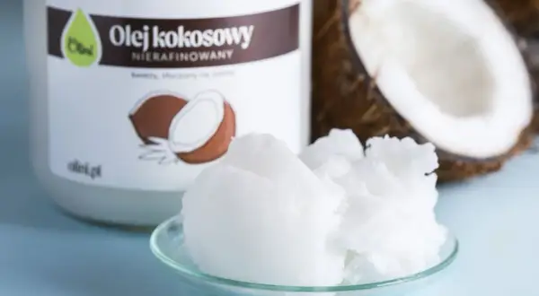 Olej kokosowy nierafinowany na talerzyku, obok słoika i połówki kokosa. Idealny do smażenia i pieczenia.