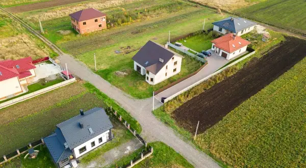 Domy na wsi, zróżnicowana odległość domu od plotu, otoczone polami i zielenią.