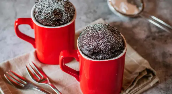Due tortine al cioccolato in tazza, spolverate di zucchero a velo, pronte per essere gustate. Una delizia veloce da preparare al microonde.