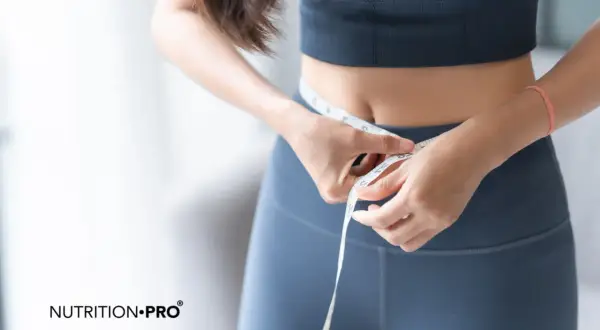 Frau misst ihre Taille. Frage: warum nehme ich trotz Sport nicht ab? Ernährung spielt eine Rolle.