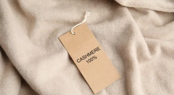Ein Etikett auf einem beigefarbenen Pullover erklärt, woraus Kaschmir besteht: 100% Kaschmir.