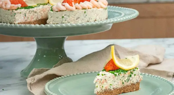 En läcker laxtårta på kavring, dekorerad med räkor, rom och citron. En bit serveras på en mintgrön tallrik.