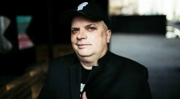Krzysztof Skiba w czapce z daszkiem i czarnej marynarce, jakby przygotowywał się do wykonania swoich kultowych utworów.