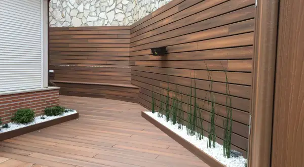 Moderna zona barbacoa exterior con tarima de madera, bancos integrados y vegetación.