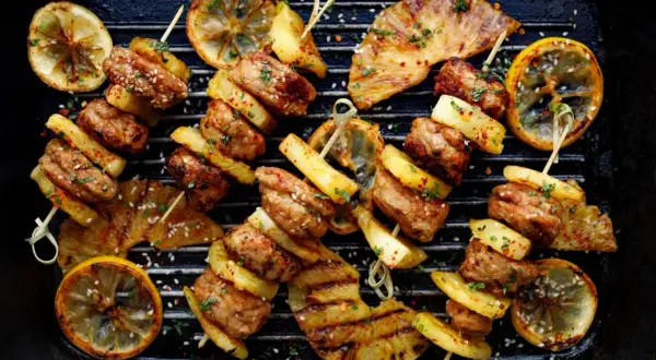 Szybkie przekąski na grilla: szaszłyki z mięsem i ananasem, grillowane cytryny i kawałki ananasa na ruszcie.