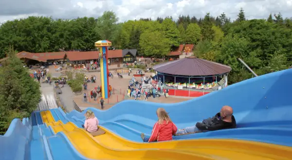 Familienrutsche im Tolk-Schau Freizeitpark mit Menschen, die rutschen und Karussell.