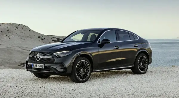 Elegancki, czarny Mercedes-Benz GLC Coupe stoi na kamienistej plaży, z widokiem na spokojne morze.