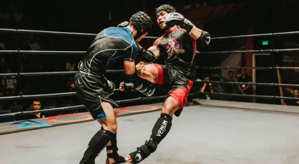 Two fighters in a ring, one delivering a powerful kick. The intensity of the moment showcases the mental fortitude and boxing psychology required for combat sports.