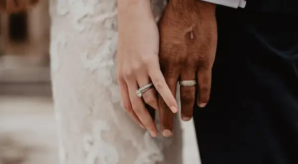 Manos entrelazadas, luciendo los anillos de casado. Ella, con un vestido de encaje, él, con traje oscuro.