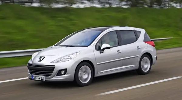 Srebrny Peugeot 207 1.6 HDI z czarnym dachem pędzi po drodze, za kierownicą siedzi mężczyzna, a obok niego pasażerka.