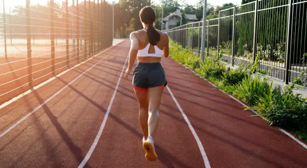 Kobieta w sportowym stroju biegnie po bieżni w słoneczny dzień.