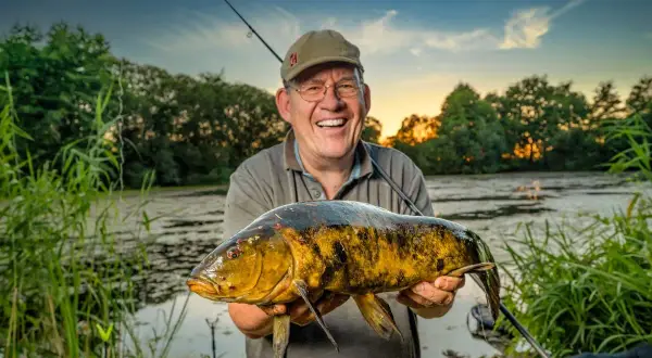 Glücklicher Angler hält großen Fisch am Lohheider See im Abendlicht.