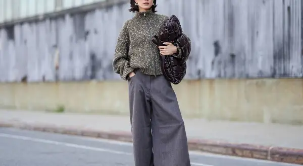 Stylisches Outfit: Eine Frau kombiniert eine graue Hose mit einem gemusterten Strickpullover und einer voluminösen Tasche.