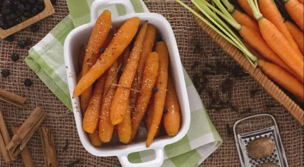 Carottes rôties dans un plat blanc, entourées d'épices : cannelle, genièvre, noix de muscade.