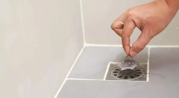 Main d'une personne retirant des cheveux du siphon pour déboucher la douche.