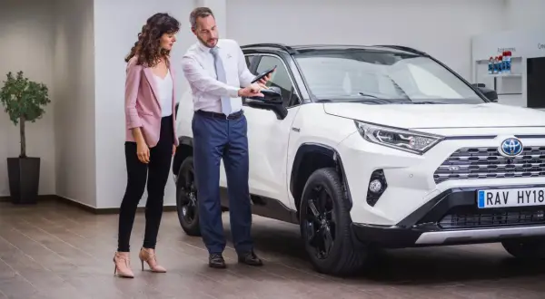 Sprzedawca pokazuje klientce detale białej Toyoty RAV4 na tablecie. To pewne auto dla wymagających.