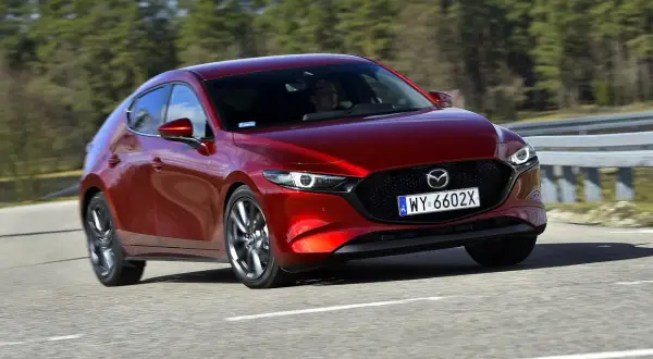 Czerwona Mazda 3 2025 na drodze, z widocznym kierowcą.