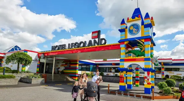 Rodzina z wózkiem spacerowym przed kolorowym hotelem Legoland Kopenhaga. Smoczy zegar i wejście z klocków LEGO.
