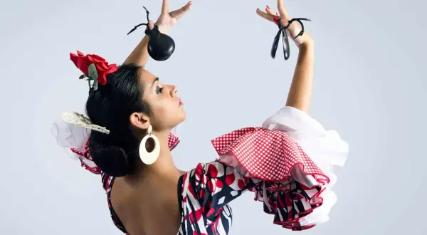 Bailarina flamenca con castañuelas y peinados sevillana, luciendo un vestido de lunares y volantes.