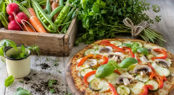 Délicieuse pizza chou fleur garnie de légumes frais, avec une caisse de radis, carottes et petits pois en arrière-plan.