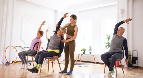 Cours de gym avec une chaise : une monitrice guide des seniors dans des étirements doux.