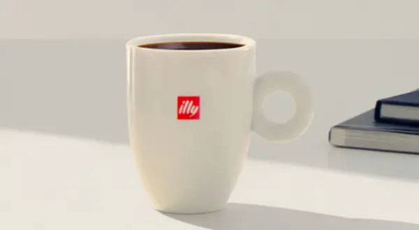 Tazza bianca con logo Illy, piena di caffè americano, pronta per una pausa studio a casa.