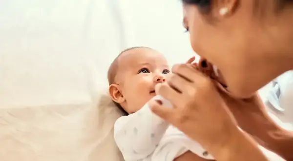 Uśmiechnięte dziecko reaguje na imię, gdy mama pochyla się, by je pocałować.