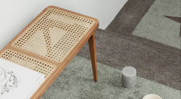 En bänk med rottingdetaljer står på ett terazzogolv. Rottingen är ett naturligt material som kan se ut som om det är på väg att ruttna om det inte sköts rätt.