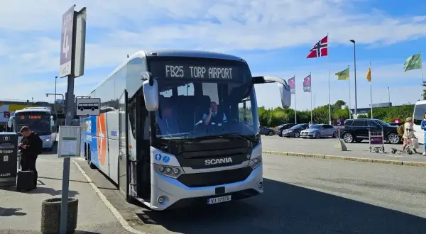 Autobus FB25 Torp Airport czeka na pasażerów. W tle parking i norweskie flagi.