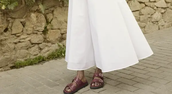 Czerwone sandałki na płaskiej podeszwie idealnie pasują do zwiewnej, białej sukienki. Oto inspiracja, jakie buty do eleganckiej sukienki wybrać na co dzień.