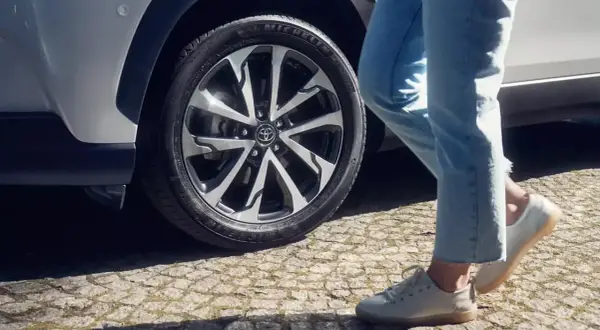 Osoba w jeansach i białych butach zbliża się do Toyoty Corolli. Dowiedz się, jak zresetować czujnik ciśnienia w oponach w tym modelu.