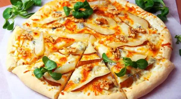 Pyszna pizza z gruszką i serem pleśniowym, posypana orzechami włoskimi i udekorowana świeżą rukolą.