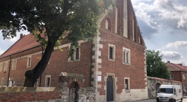 Stary ceglany budynek z kamiennymi detalami, otoczony murem i drzewem. To jedna z kazimierza wielka atrakcji, gdzie historia spotyka się z teraźniejszością.