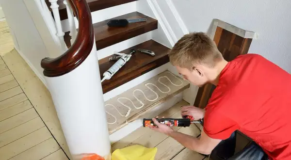 Man renoverar trappa med fogpistol och lim på trappsteg. Nya golvbrädor ligger redo.