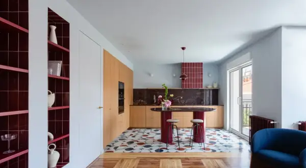 Cocina moderna con isla ovalada, estanterías rojas y suelo geométrico. Un ejemplo de **estudios interiorismo** audaces y coloridos.